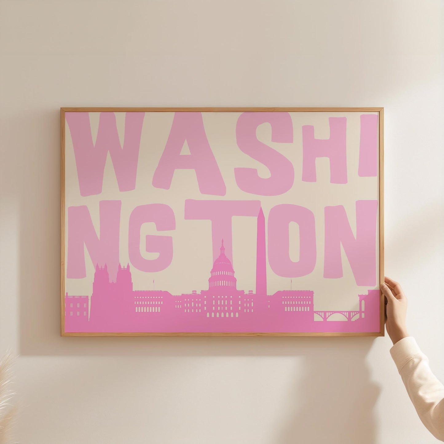 A modern graphic print of the Washington DC skyline in shades of pink. The word 'WASHINGTON' is in large light pink letters above the cityscape.