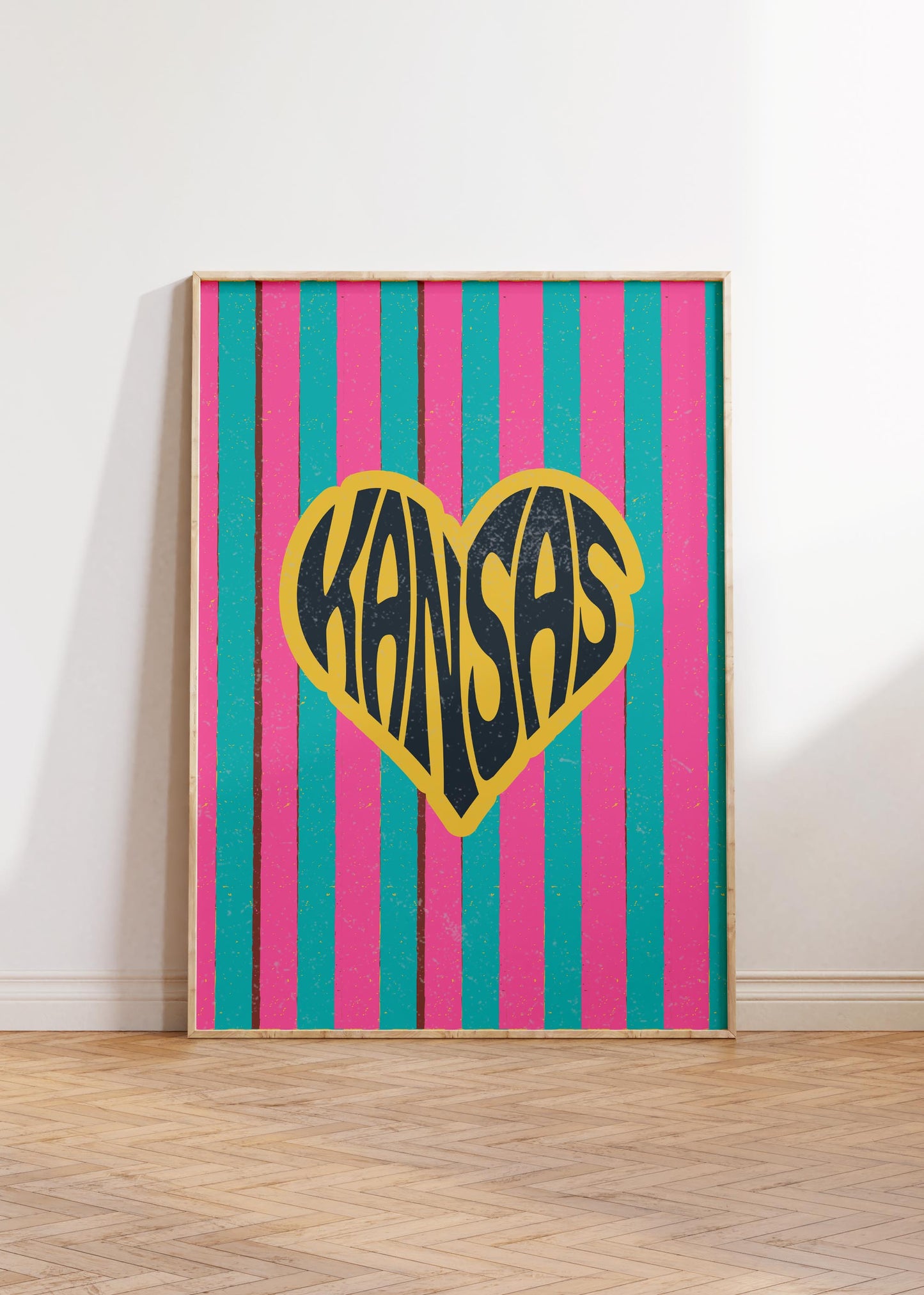 A heart-shaped design with the word 'Kansas' in groovy black retro font, outlined in yellow, set against a background of vertical pink and teal stripes.