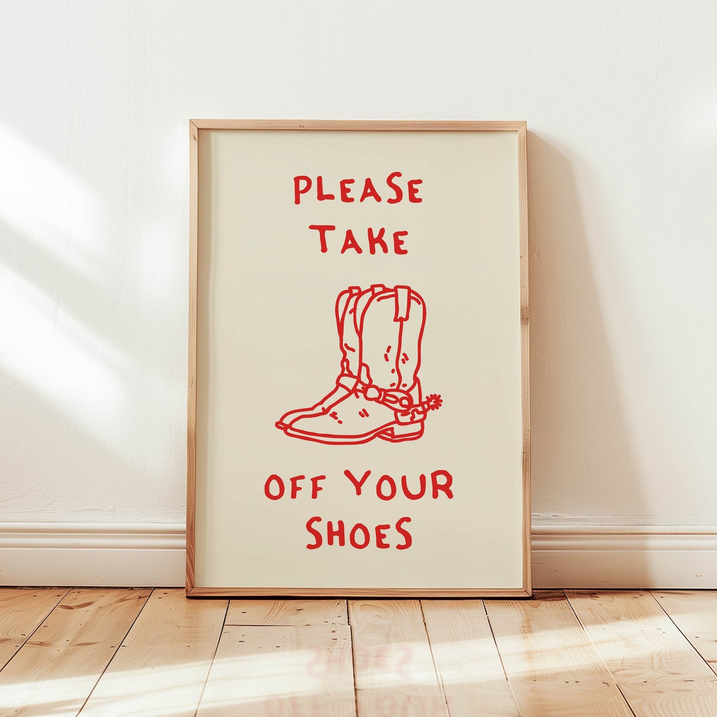 A 'Take Off Your Shoes' sign featuring a red line drawing of cowboy boots, framed and leaning against a wall as entryway decor.