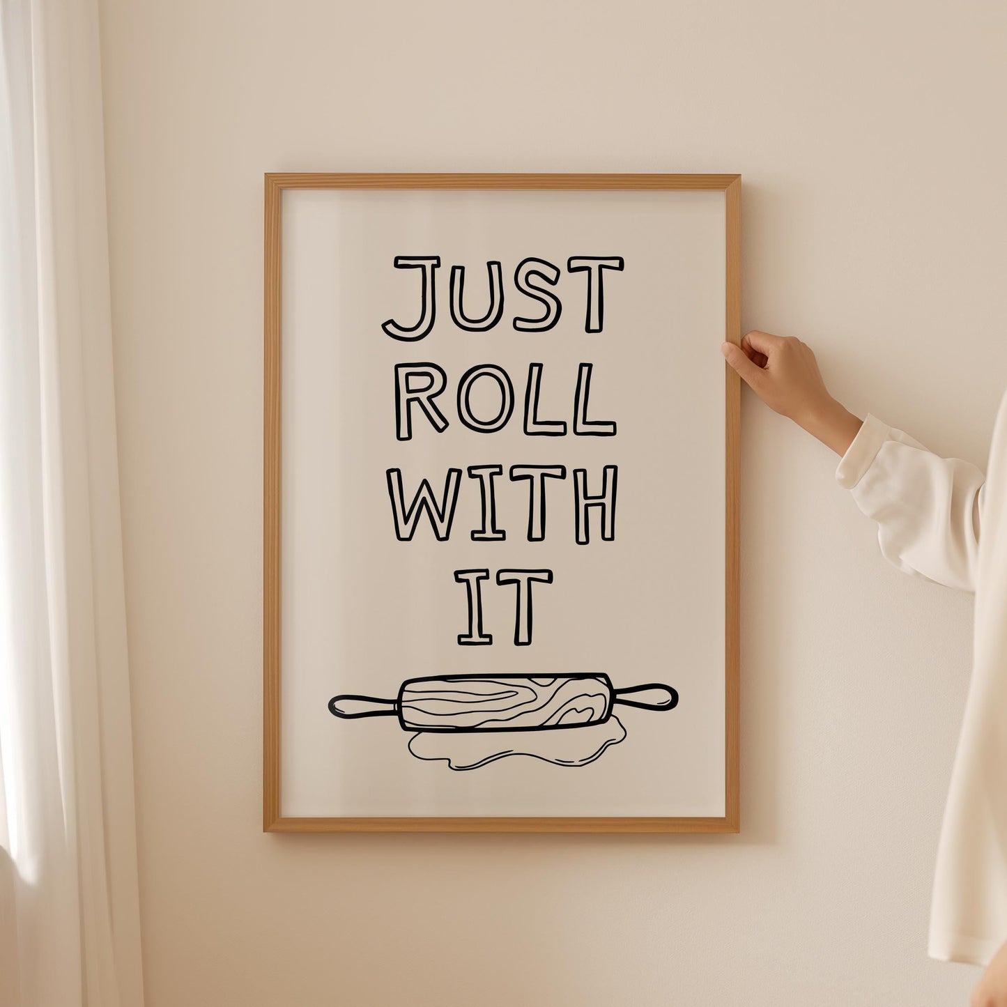 A framed kitchen wall art print with the quote 'Just roll with it' above a hand-drawn illustration of a rolling pin and dough.