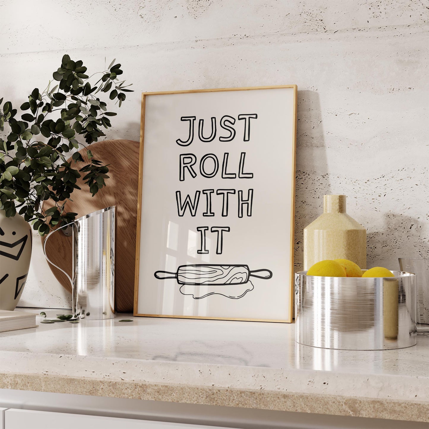 A framed kitchen wall art print with the quote 'Just roll with it' above a hand-drawn illustration of a rolling pin and dough.