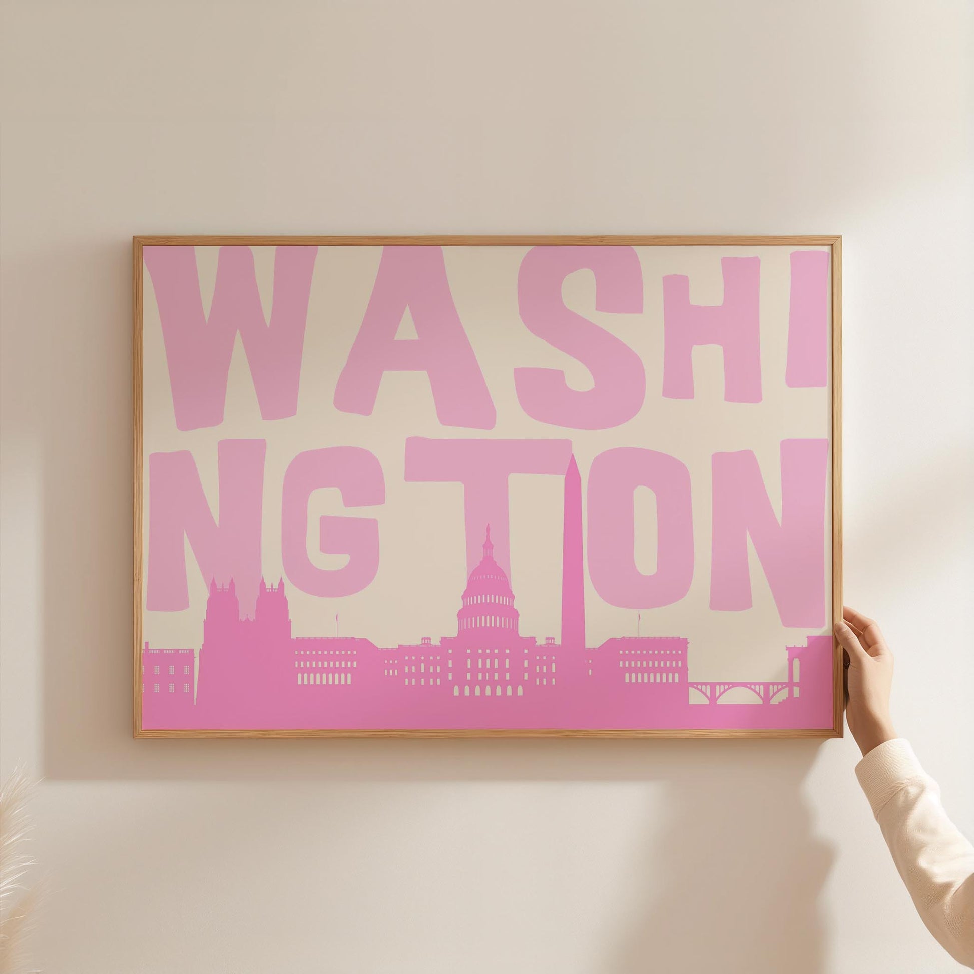 A modern graphic print of the Washington DC skyline in shades of pink. The word 'WASHINGTON' is in large light pink letters above the cityscape.