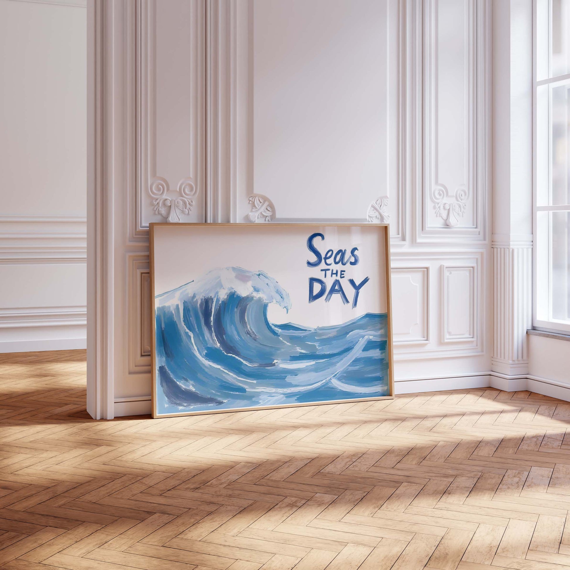 A coastal wall art print in a landscape frame, featuring a large, painterly blue ocean wave and the quote 'Seas the Day'.
