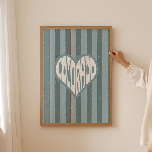 Colorado written in white text inside a heart shape on a background of vertical muted blue and brown stripes.