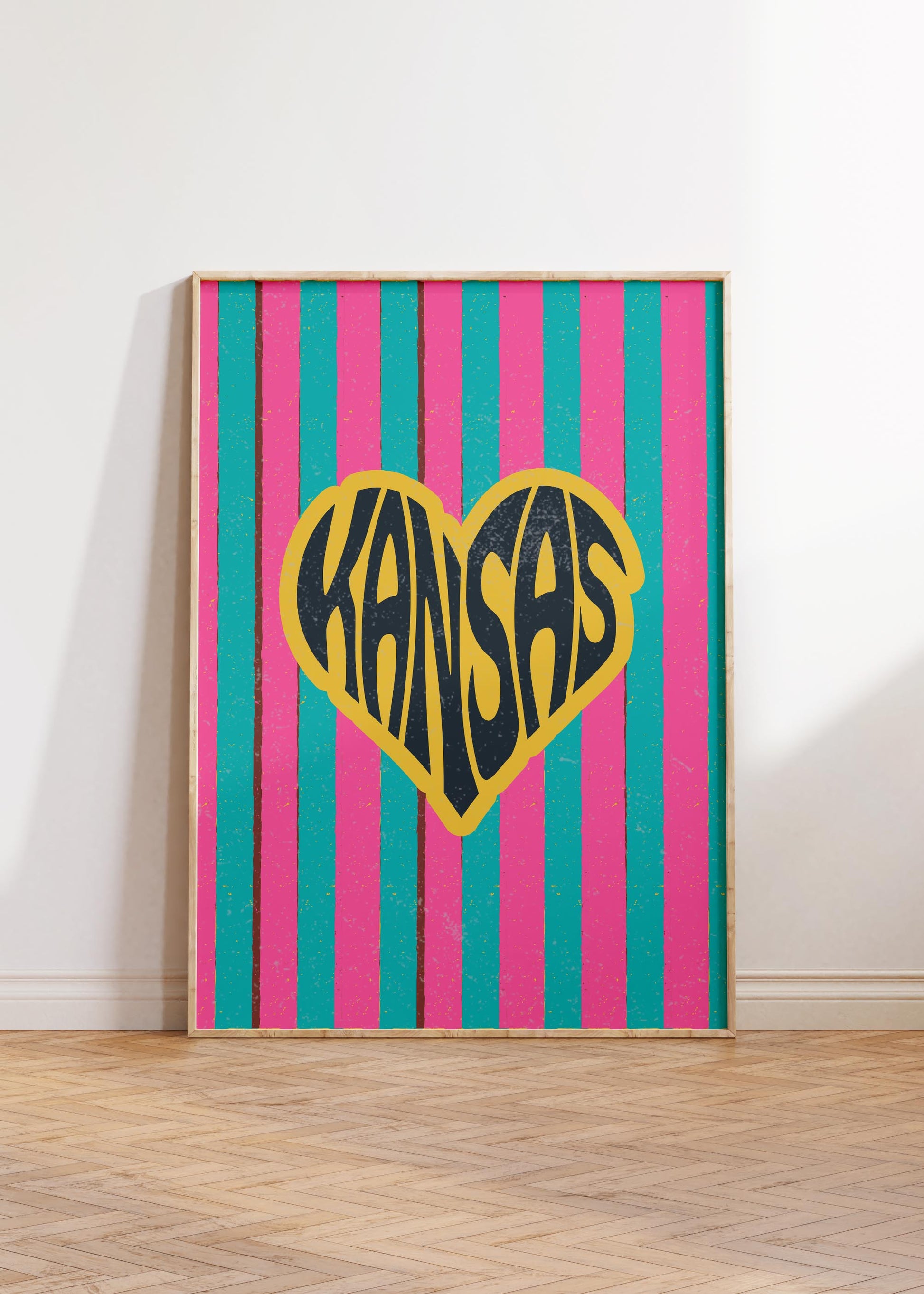 A heart-shaped design with the word 'Kansas' in groovy black retro font, outlined in yellow, set against a background of vertical pink and teal stripes.