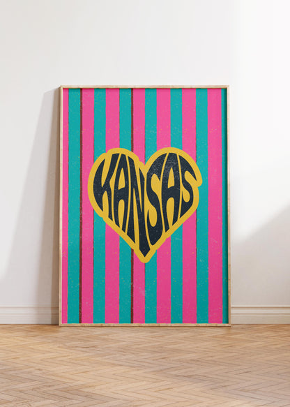 A heart-shaped design with the word 'Kansas' in groovy black retro font, outlined in yellow, set against a background of vertical pink and teal stripes.