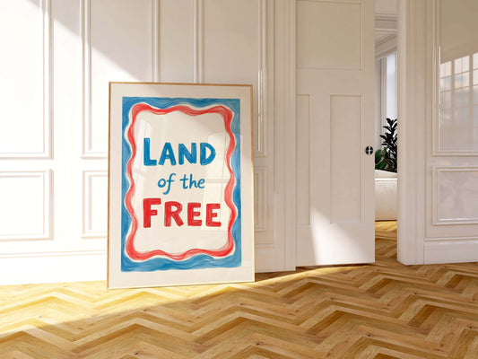A framed 4th of July print with the words 'Land of the Free' in blue text, surrounded by a wavy red and blue border.