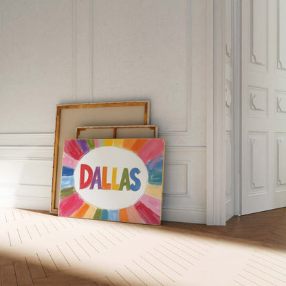 A colorful Dallas print in a landscape frame, with the word 'DALLAS' in rainbow letters surrounded by a painterly sunburst of color.