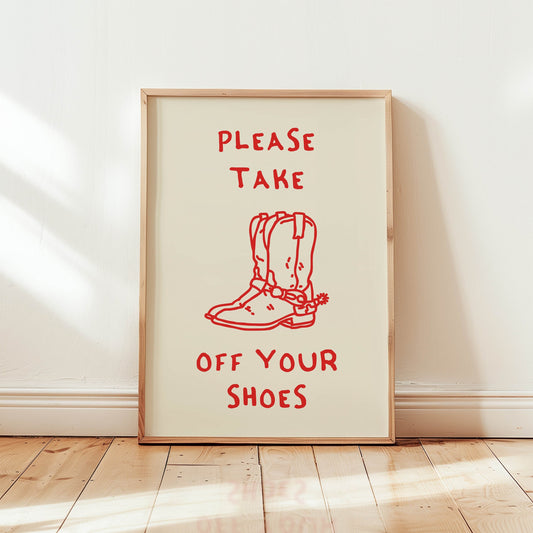 A 'Take Off Your Shoes' sign featuring a red line drawing of cowboy boots, framed and leaning against a wall as entryway decor.