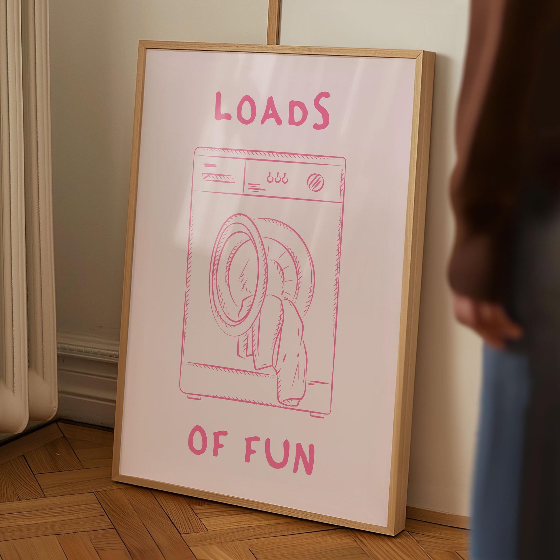 Framed funny laundry room print with a pink washing machine illustration and the pun 'Loads of Fun' on a pink background.