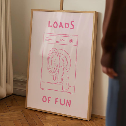 Framed funny laundry room print with a pink washing machine illustration and the pun 'Loads of Fun' on a pink background.