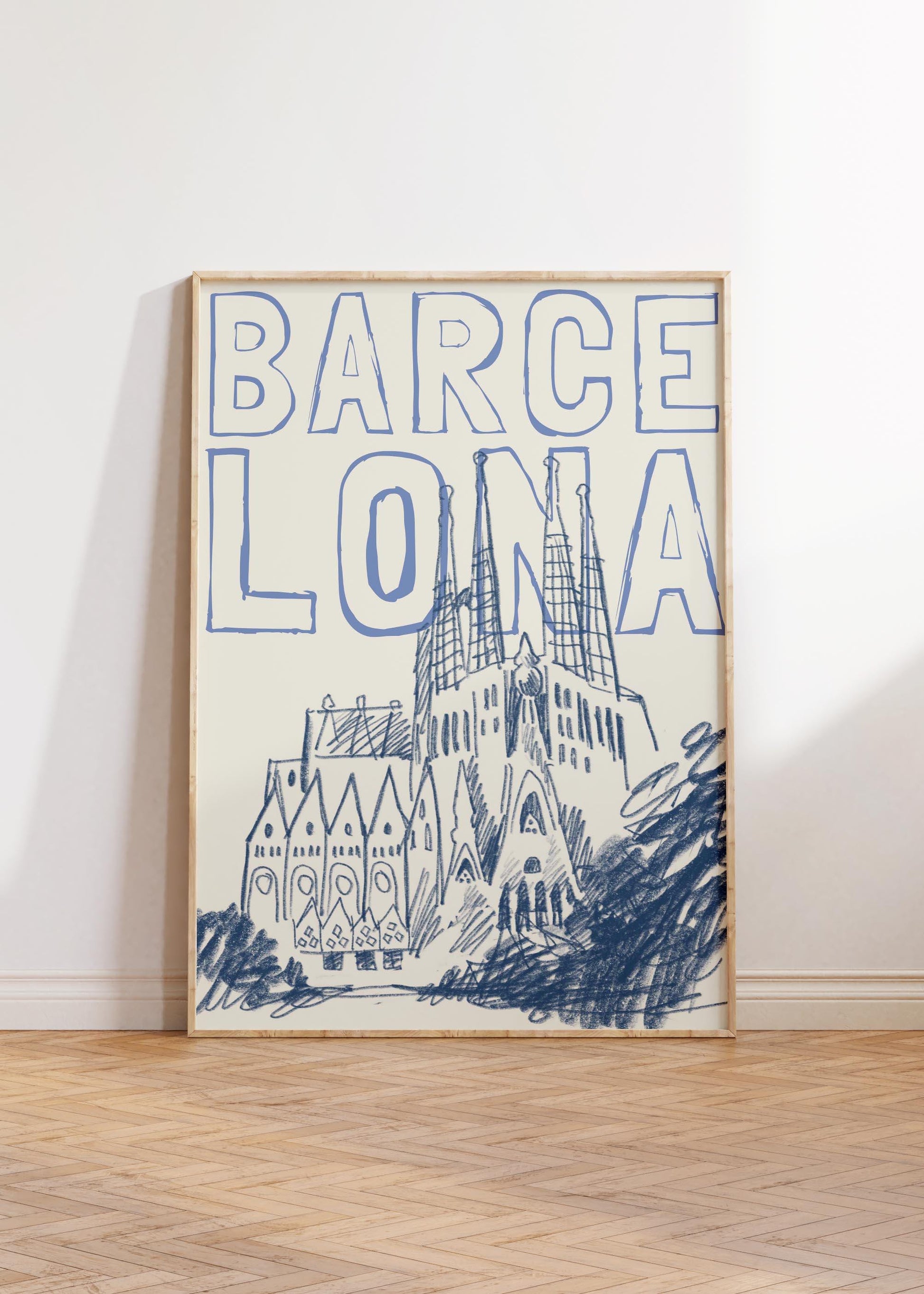 A Barcelona travel poster in a wood frame, with a blue sketch of the Sagrada Familia and the word 'BARCELONA' in a block font.
